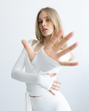 Woman in a white outfit with long sleeves and gloves against a light gray background