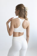 Woman wearing a white sports bra and leggings on a light gray background