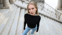Model wearing black long-sleeve wrap top and light blue leggings standing on stone stairs.