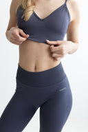 Person wearing a dark blue sports bra and leggings on a light background