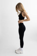 Woman wearing a black sports bra and leggings on a white background