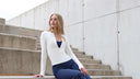 Woman sitting on concrete steps wearing a white top and blue pants.